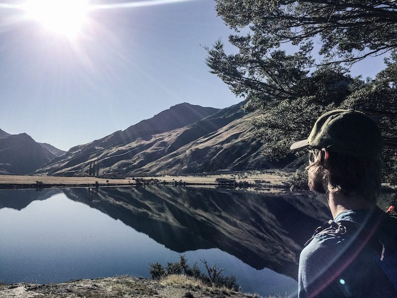 Man in baseball hat looking at mountain with reflection on the water