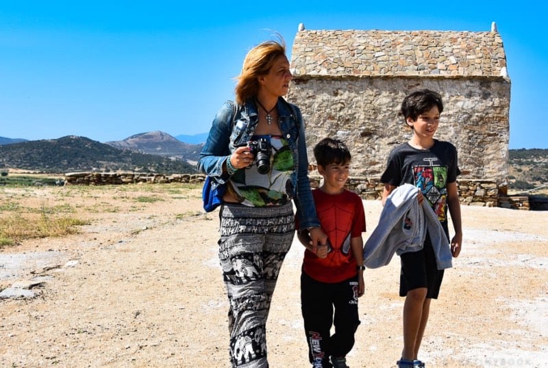 mom with camera and 2 sons walking in front of stone house: multicultural kids