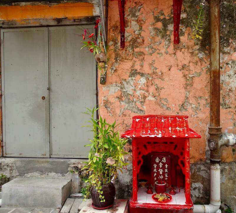 red Chinese shrine against a crumbling peach wall, Penang where to stay