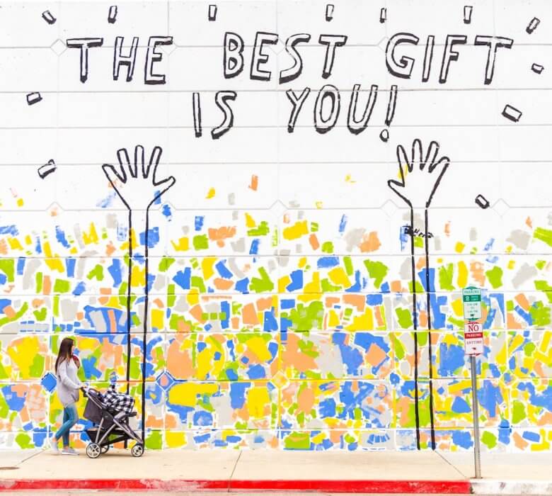 woman walking in front of mural that says the best gift is you