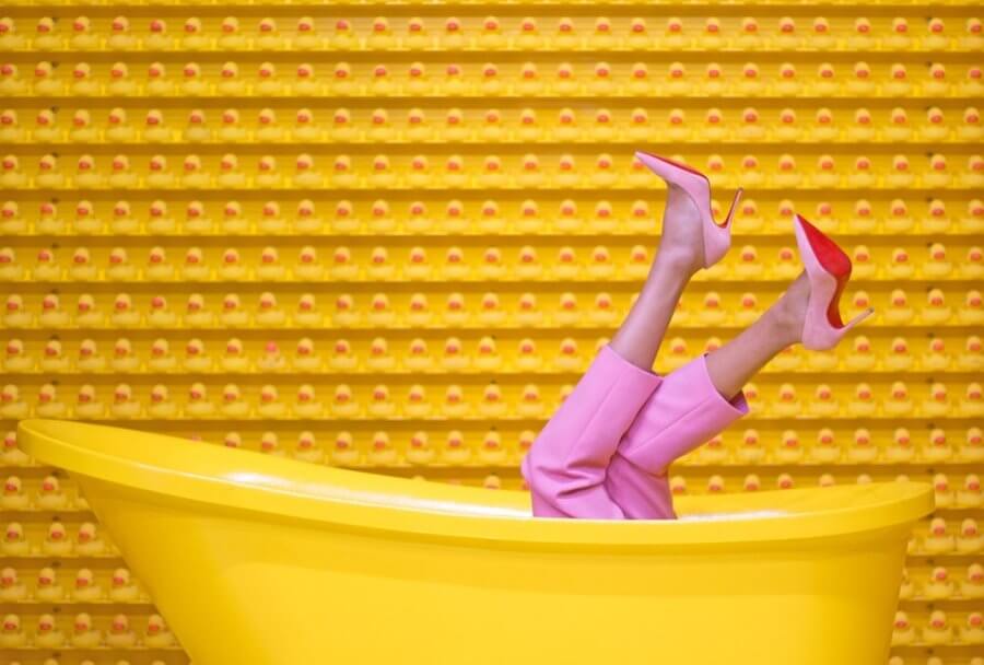 yellow background, legs in pink pants and heels popping out of tub.