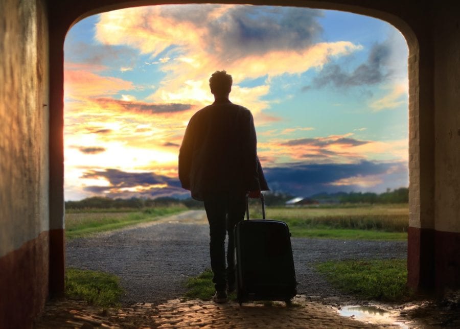 man walking with suitcase into sunset