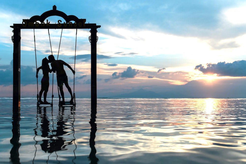 silhouette of couple kissing on swings over water