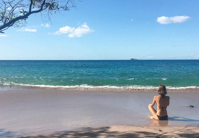 Emily sitting in the sand, staring at the ocean, on a Costa Rica beach. Reasons to move to another country