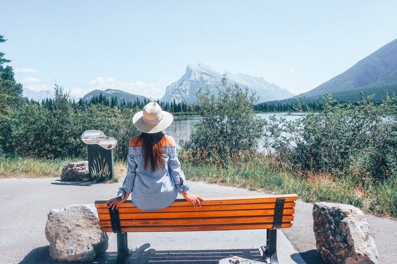 Girl in cowboy hat sitting on bench looking at a Canadian landscape. Reasons to move to another country.