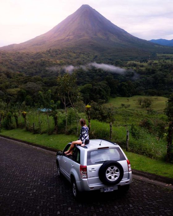 Girl sitting on car looking at Arenal Volcano, Costa Rica
