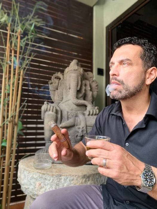 Dark haired man smoking a cigar in front of Ganesh