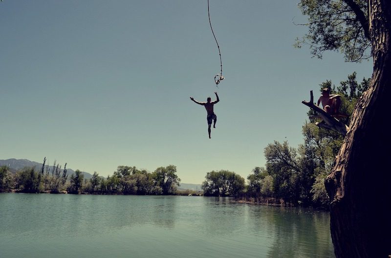 guy letting go of rope swing over water. 