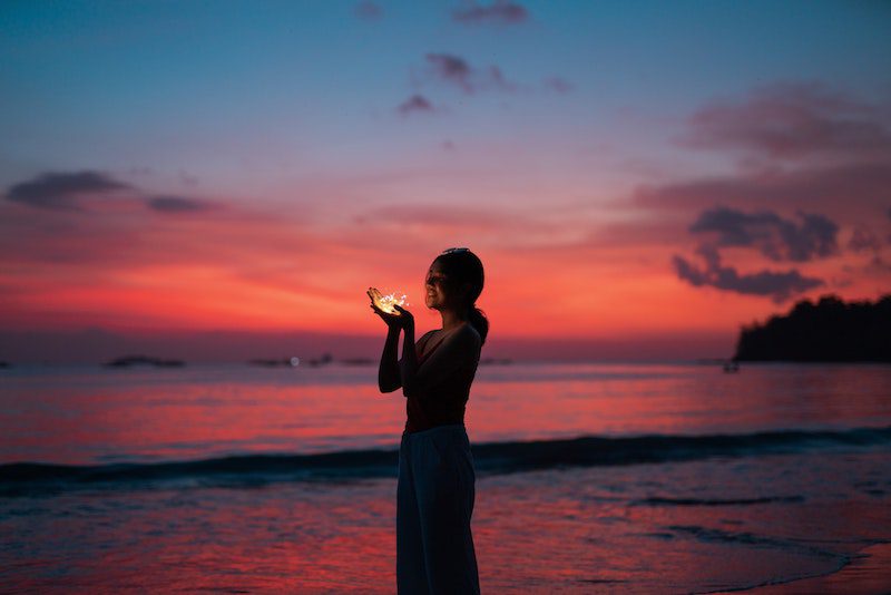woman holding fairy lights on beach at sunset