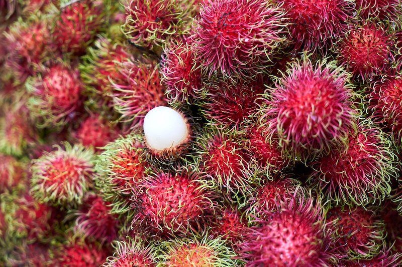 a pile of red rambutan and 1 open one. fruits of malaysia