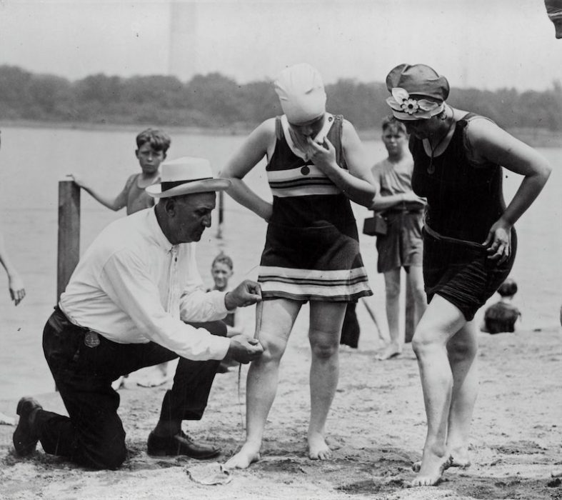 black and white picture of a man measuring the length of a swim suit in the 1930s