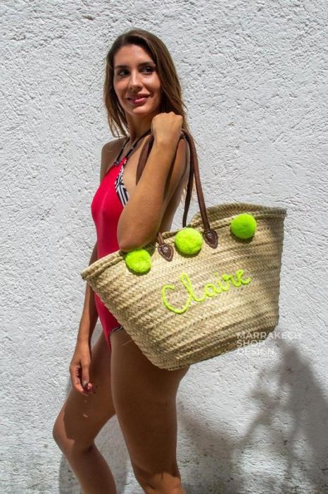 girl in red bathing suit holding a straw bag with bright green pom-poms and Claire embroidered on it. An adorable gift for beach lovers