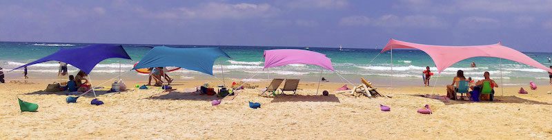 4 different colored beach shades with people sitting under them. Practical gifts for beach lovers 