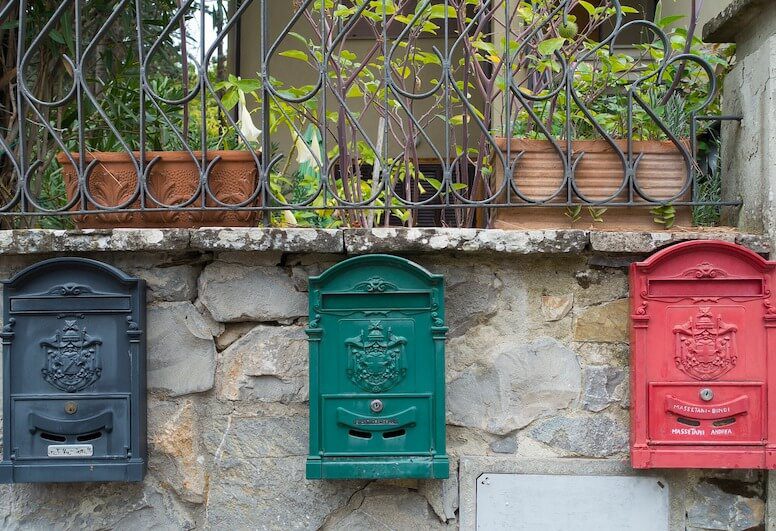 3 mailboxes: one black, green and red on a stone wall. 