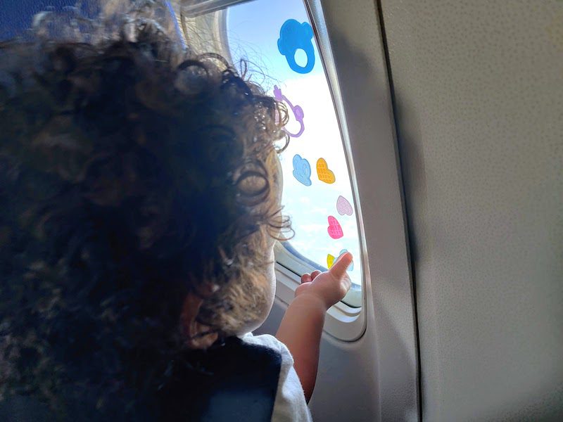 curly haired kid looking out of a plane window with stickers on it
