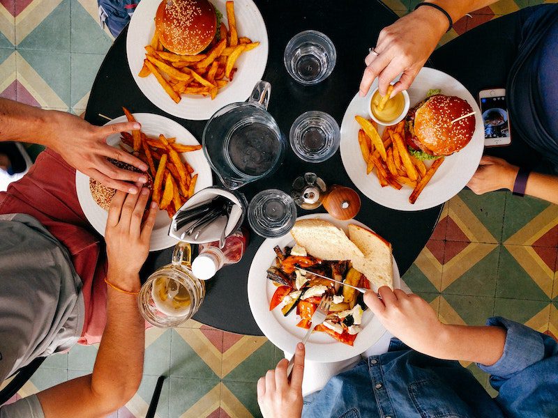 Overview of 4 plates of food, with people eating the burgers and salad.