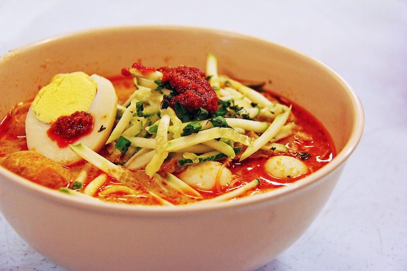 Nyonya laksa is bowl of red soup with noodles, egg and chili sauce. 