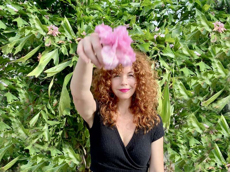 redhead holding pink flower in front of green wall