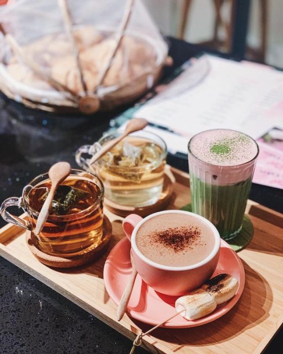 four drinks: 2 teas in glass mugs, 1 coffee in a pink cup and one pink and green tall drink