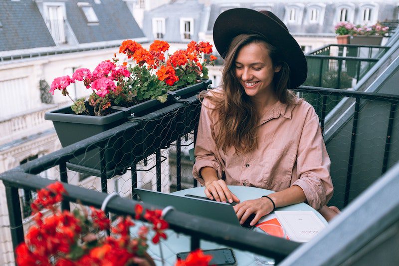 woman working her job for digital nomad on a balcony with red flowers