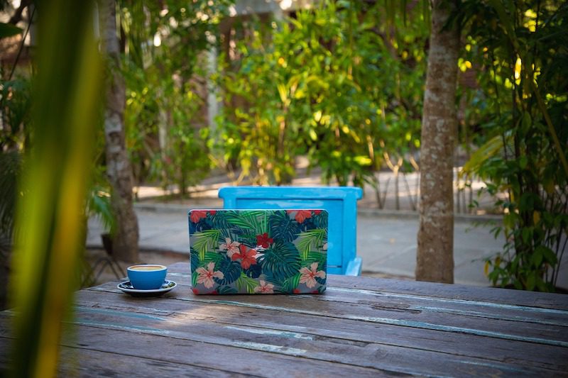 laptop with a tropical cover with a cup of coffee next to it. Work outside as a digital nomad