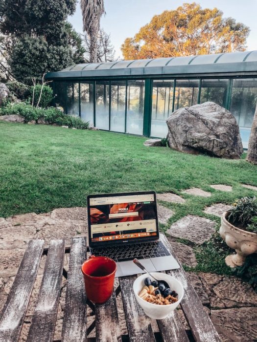 laptop with a bowl of fruit and coffee outside on a wooden table near a green lawn