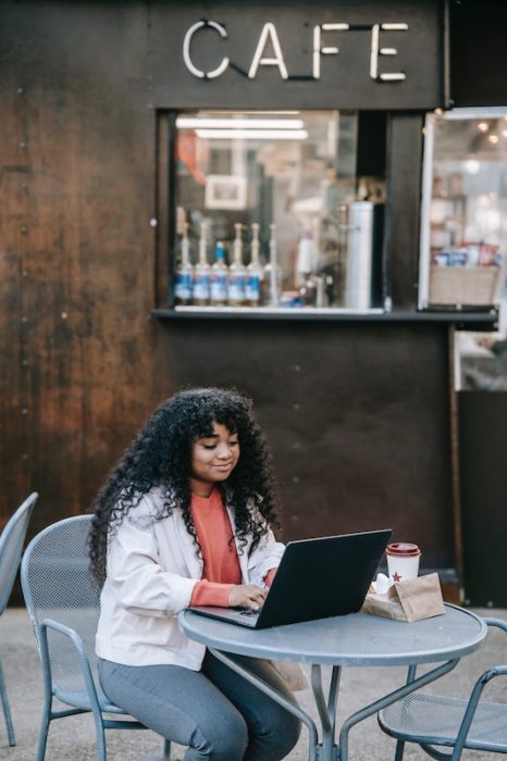 black woman with a laptop working from a cafe. Digital nomad jobs mean you can work from anywhere
