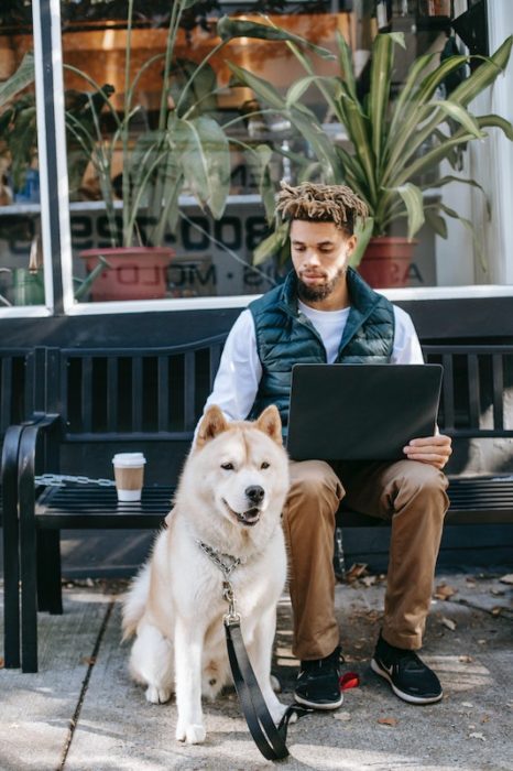  black man with short dreads sitting with fluffy white dog and laptop on a bench. Jobs for digital nomads mean you can work everywhere

