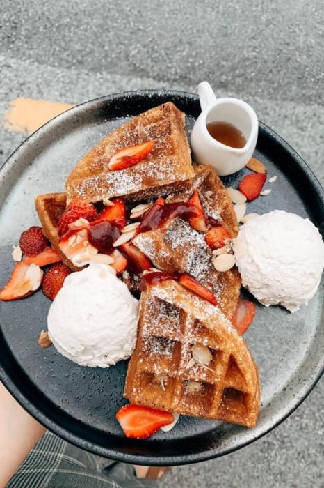 waffles covered in strawberries almonds and 2 scoops of ice cream. 