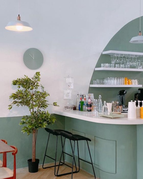 cafe with sage green walls and clock near a bar