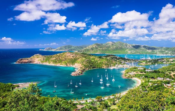 Antigua landscape with green hills and sailboats in the blue ocean. If you were on a remote visa this could be your view.