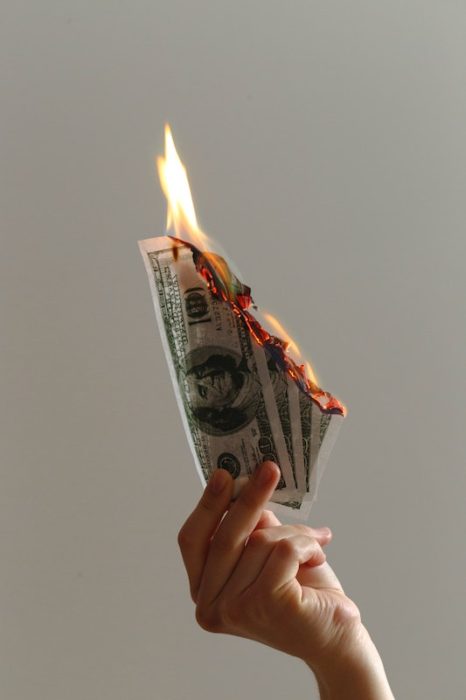 hand holding US dollar bills and burning them