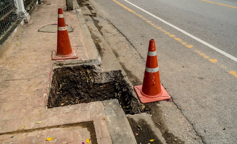 hole in sidewalk with two orange cones