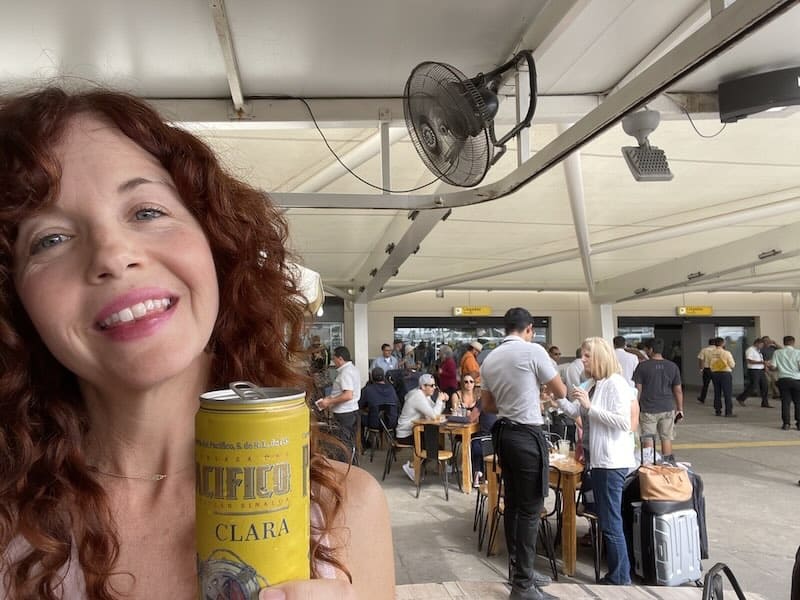 girl holding a Pacifico in front of people waiting at the Puerto Vallarta Airport